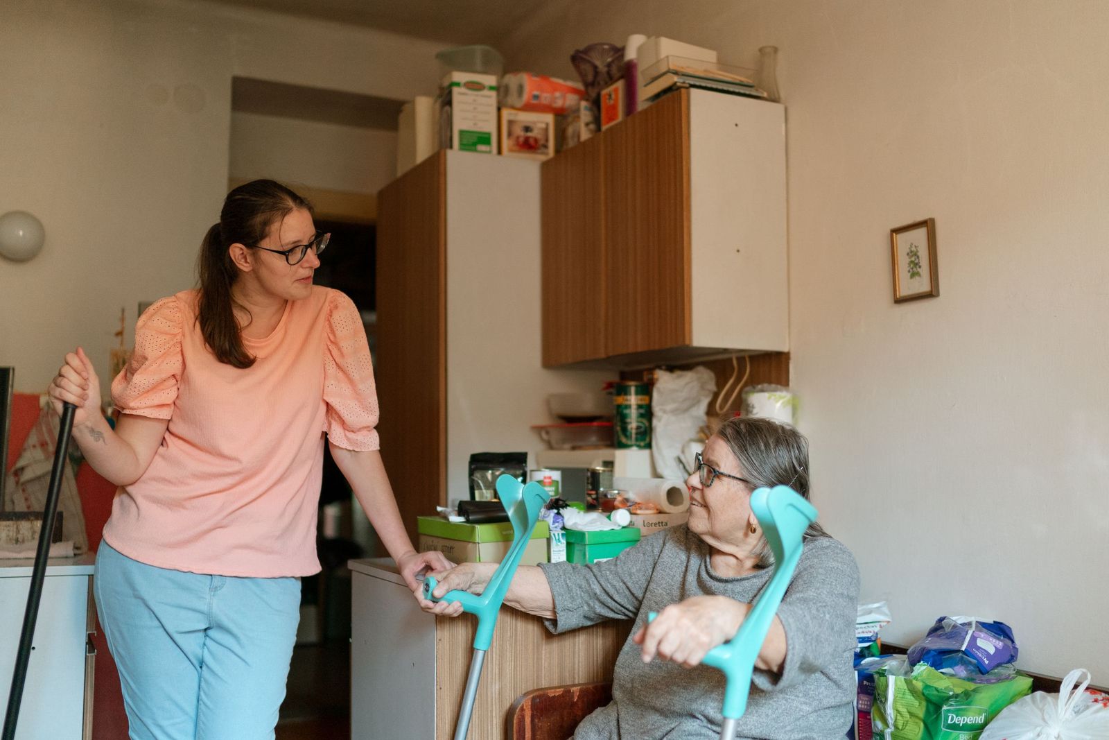 Caregiver helping an older woman walk with crutches at home